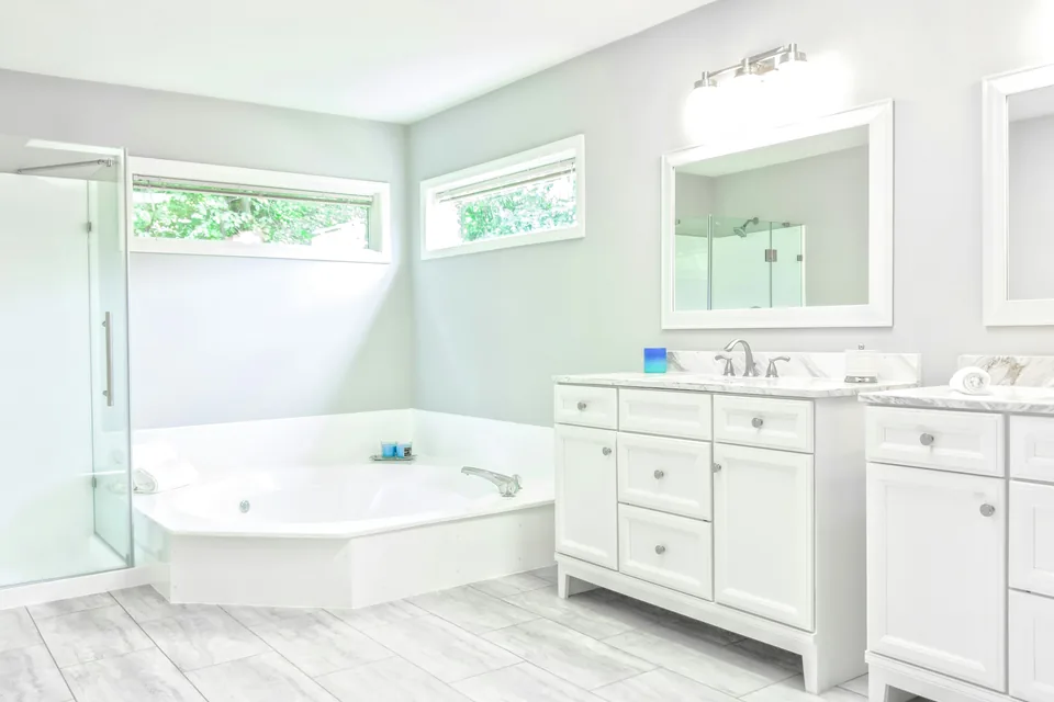 Bright bathroom with a corner tub, glass shower, white vanity and wall lighting