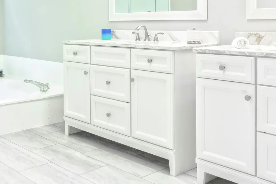 Close view of a pale veined bathroom counter, silver-tone faucet and white vanity above gray floor tiles
