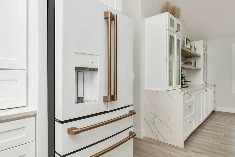 Close view of gold-tone refrigerator handles and nearby white cabinet pulls