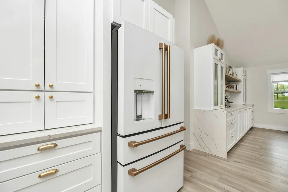 White kitchen cabinets with gold-tone pulls, pale veined counters and a wood-look floor